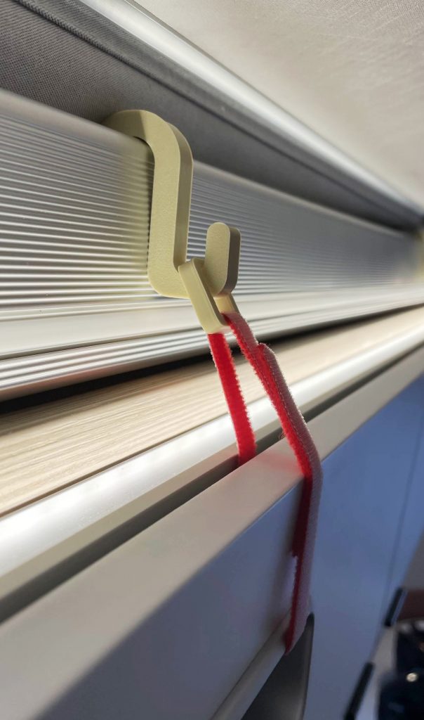 Die Schranksicherung im Einsatz: sie wird im Alurahmen des Daches eingehängt, das Klettband als Schlaufe durch die Griff-Öffnung der Klappe des Hängeschrankes geführt und mit der Öse im Haken eingehängt. 